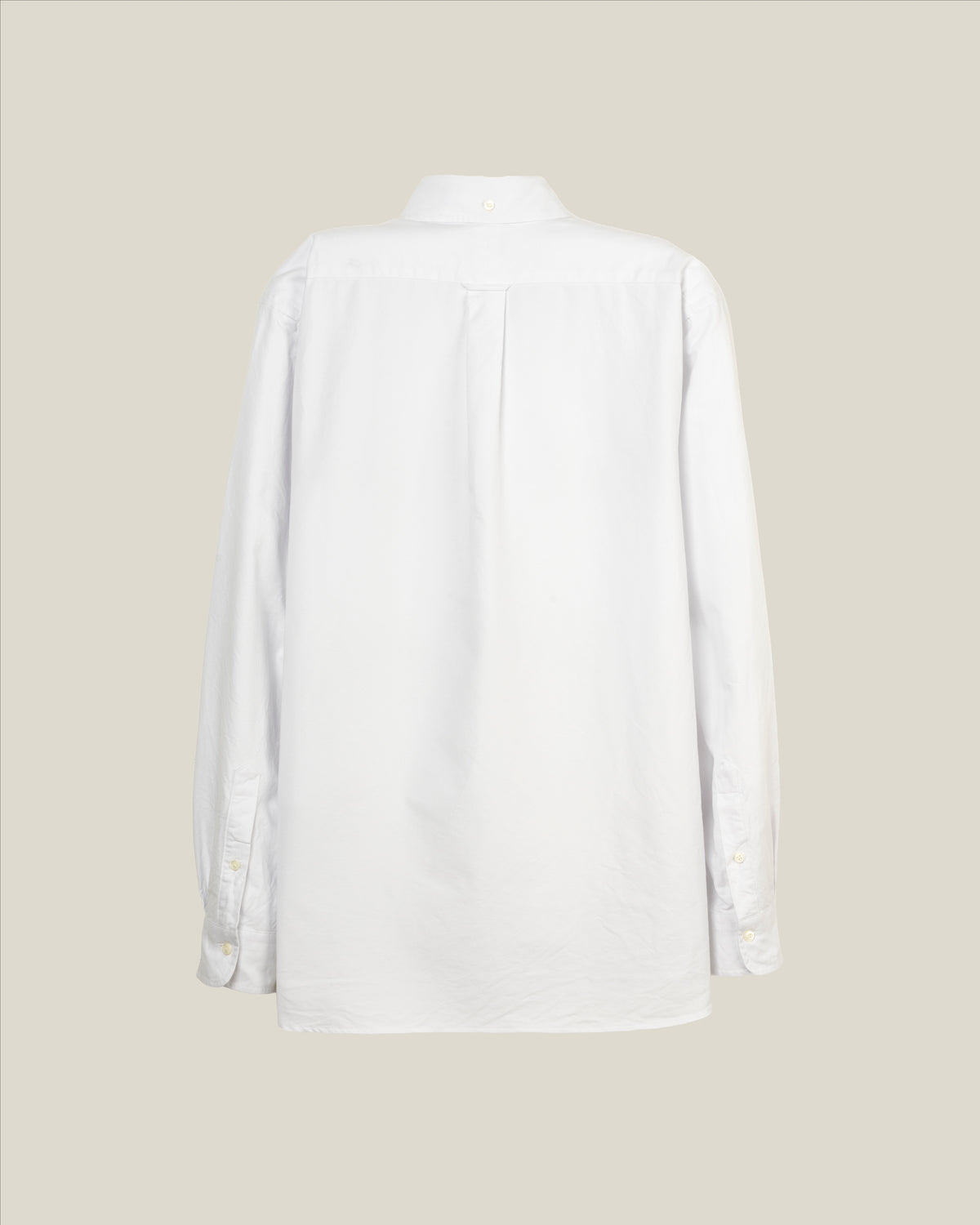 A white long-sleeve button-up shirt shown from the back, featuring a subtle vertical pleat down the center back, set against a solid light beige background.  Made in USA Oxford Cloth Button Down