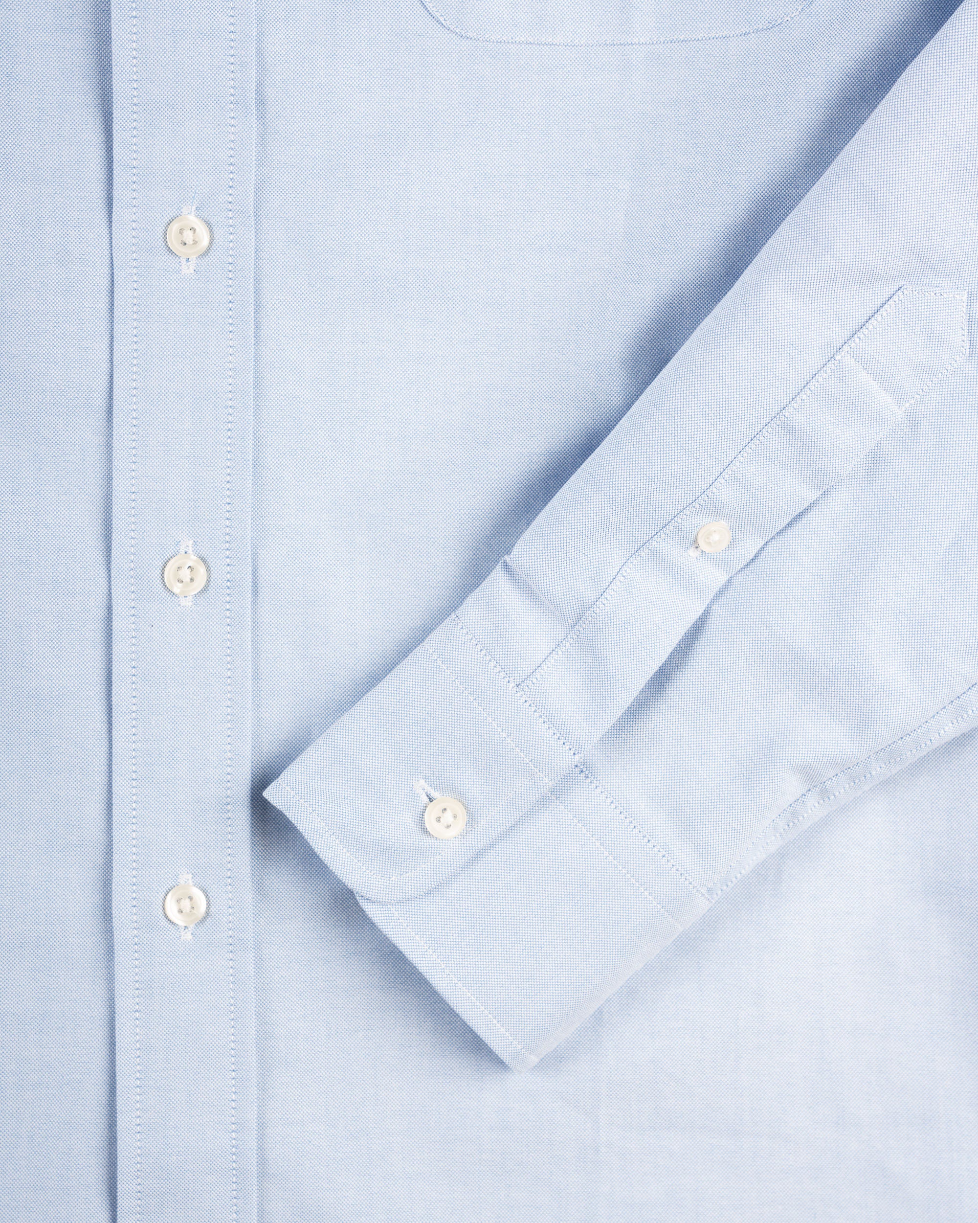 Close-up of a light blue shirt with button details of the arm length and construction.